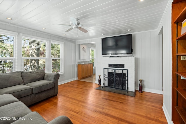 living area featuring light wood finished floors, ornamental molding, a brick fireplace, ceiling fan, and baseboards