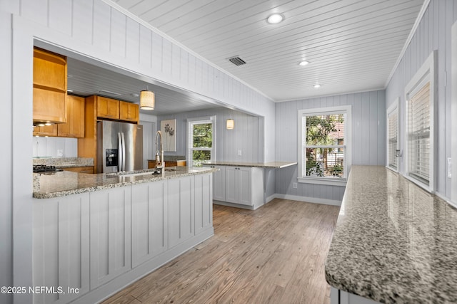 kitchen featuring stainless steel fridge with ice dispenser, ornamental molding, light stone counters, light wood-type flooring, and white cabinetry