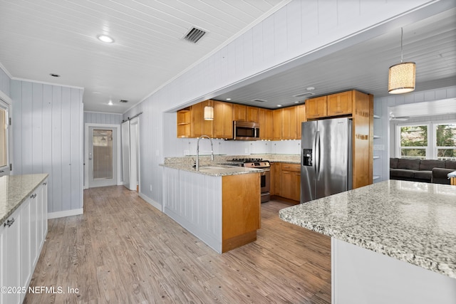 kitchen with stainless steel appliances, a barn door, hanging light fixtures, and light stone countertops