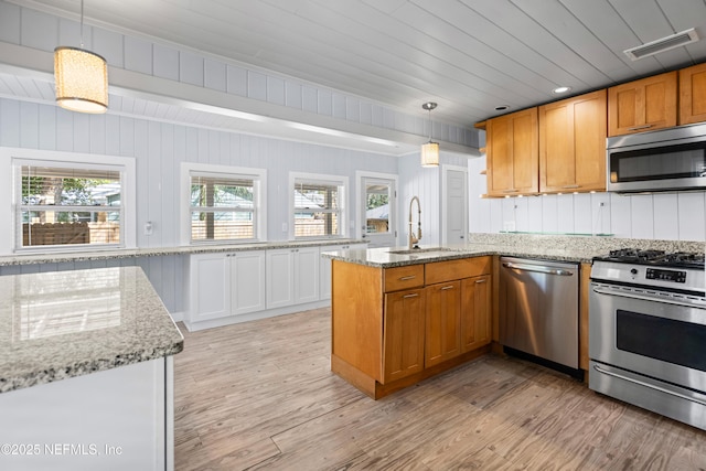 kitchen featuring light stone counters, pendant lighting, visible vents, appliances with stainless steel finishes, and a sink