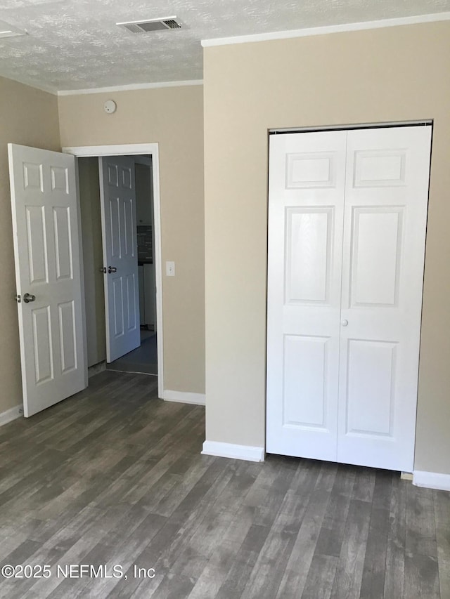 unfurnished bedroom with a textured ceiling, visible vents, a closet, dark wood finished floors, and crown molding