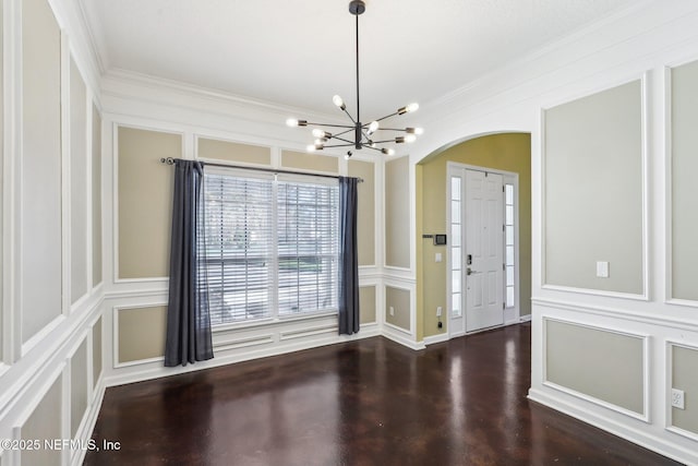 entryway featuring ornamental molding, arched walkways, a decorative wall, and an inviting chandelier