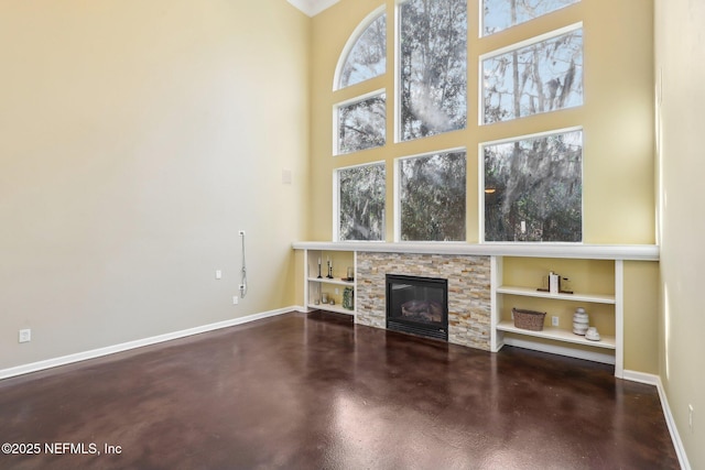 unfurnished living room featuring a stone fireplace, concrete floors, a towering ceiling, and baseboards