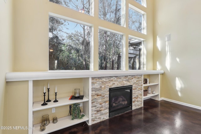 living room featuring concrete floors, a fireplace, a towering ceiling, and baseboards