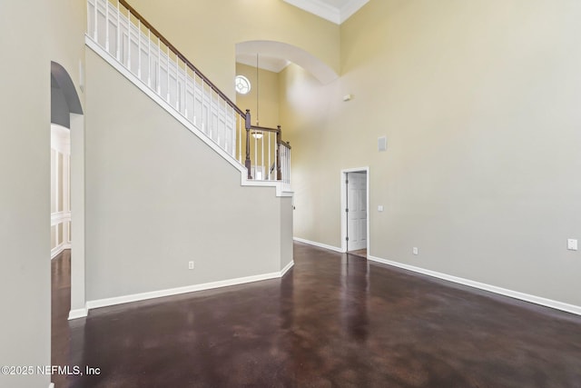 unfurnished living room featuring arched walkways, a high ceiling, concrete floors, baseboards, and stairs