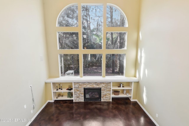 unfurnished living room featuring finished concrete flooring, a fireplace, a wealth of natural light, and baseboards