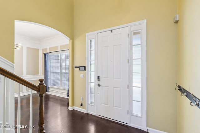 foyer with arched walkways, stairs, dark wood finished floors, and baseboards