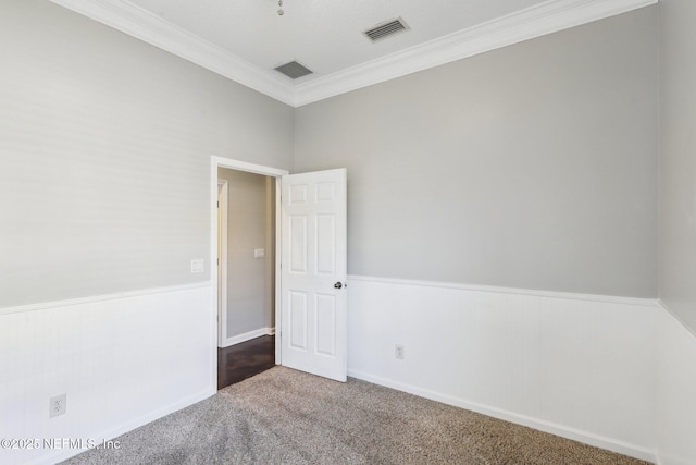 empty room with a wainscoted wall, ornamental molding, carpet, and visible vents