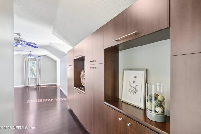 hall with dark wood-style flooring, vaulted ceiling, a textured ceiling, and baseboards