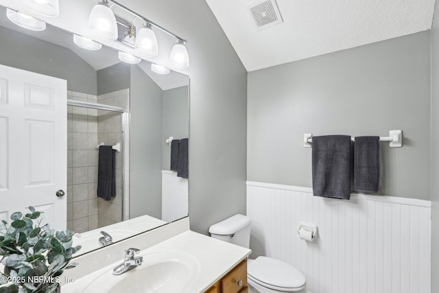 bathroom featuring visible vents, tiled shower, wainscoting, toilet, and vanity