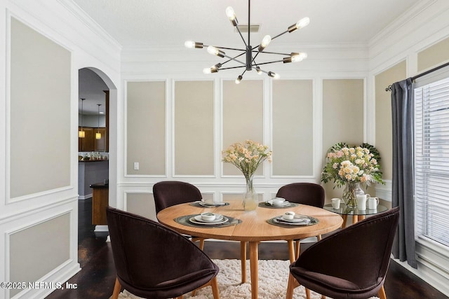 dining space featuring dark wood-style floors, ornamental molding, and a decorative wall