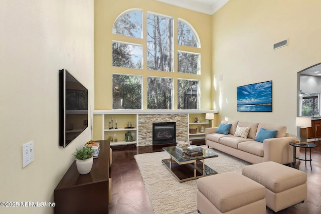 living room featuring crown molding, visible vents, a fireplace, and a towering ceiling