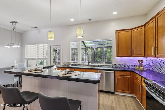 1494 Walnut Creek Dr, Fleming Island, FL 32003 - kitchen featuring stainless steel dishwasher, dark countertops, light wood finished floors, a breakfast bar, and brown cabinets