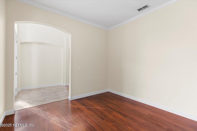 spare room with arched walkways, wood finished floors, visible vents, baseboards, and ornamental molding