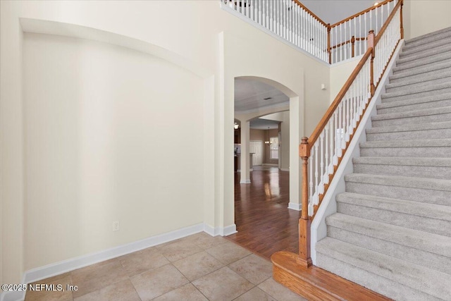 entryway featuring arched walkways, a towering ceiling, baseboards, stairs, and tile patterned floors