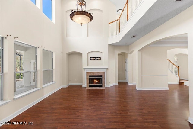 unfurnished living room featuring visible vents, stairway, a tiled fireplace, wood finished floors, and baseboards