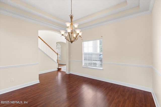 empty room featuring arched walkways, wood finished floors, baseboards, stairs, and a raised ceiling