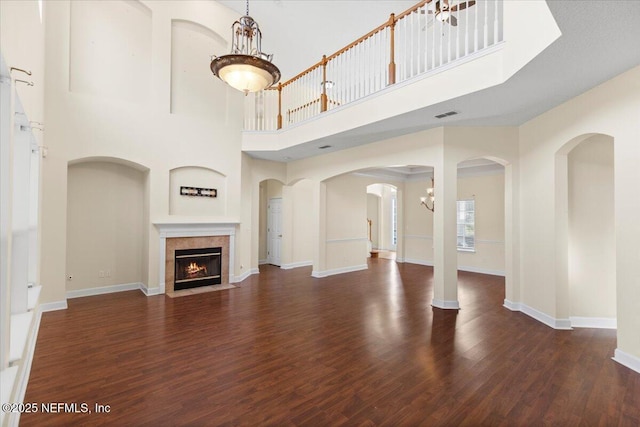 unfurnished living room featuring baseboards, visible vents, a towering ceiling, a fireplace with flush hearth, and wood finished floors