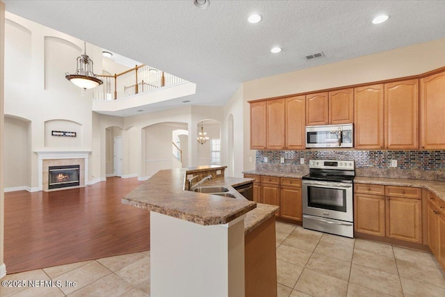 kitchen featuring light tile patterned floors, stainless steel appliances, visible vents, tasteful backsplash, and a glass covered fireplace