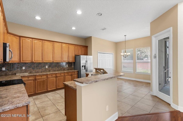 kitchen featuring a notable chandelier, stainless steel appliances, decorative backsplash, a sink, and an island with sink