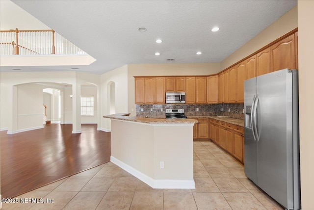 kitchen with light tile patterned floors, stainless steel appliances, a peninsula, and backsplash