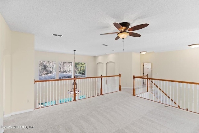 carpeted empty room with a textured ceiling, visible vents, a ceiling fan, and baseboards