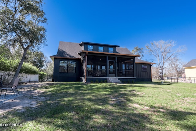 back of house with board and batten siding, a sunroom, a fenced backyard, and a lawn