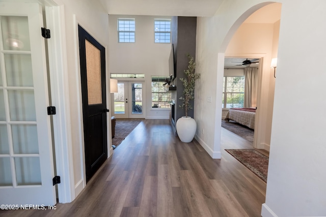 entrance foyer featuring arched walkways, french doors, a towering ceiling, wood finished floors, and baseboards