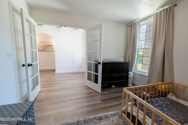 bedroom with arched walkways, french doors, wood finished floors, and baseboards