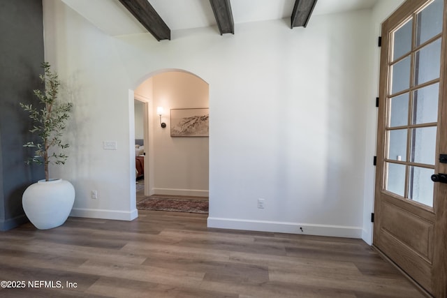 interior space featuring baseboards, arched walkways, wood finished floors, and beamed ceiling