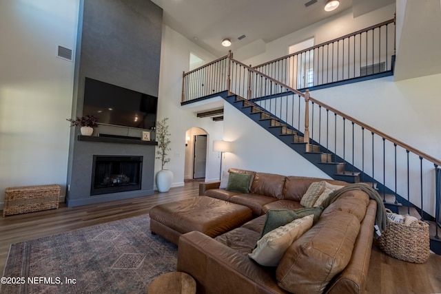 living room featuring visible vents, arched walkways, a towering ceiling, wood finished floors, and a fireplace