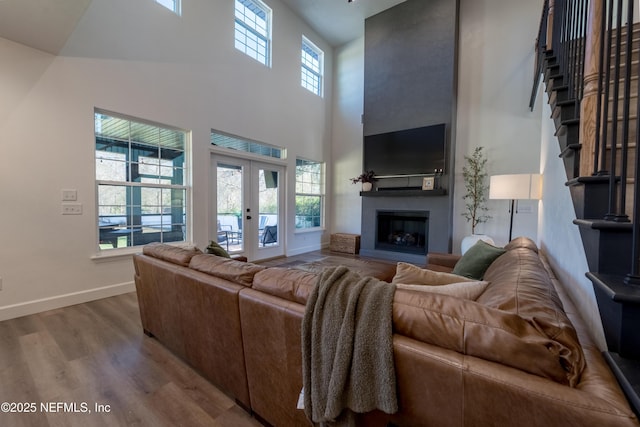 living area with a fireplace, wood finished floors, a towering ceiling, baseboards, and french doors