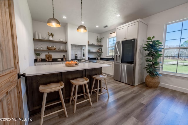 kitchen featuring open shelves, stainless steel fridge with ice dispenser, a kitchen breakfast bar, wood finished floors, and pendant lighting