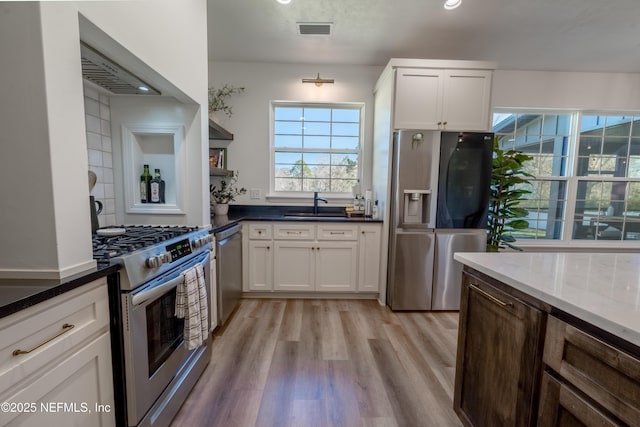 kitchen featuring visible vents, appliances with stainless steel finishes, light wood-type flooring, white cabinetry, and a sink