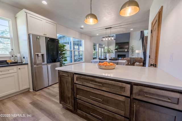 kitchen featuring white cabinets, stainless steel fridge with ice dispenser, hanging light fixtures, light wood-style floors, and a fireplace