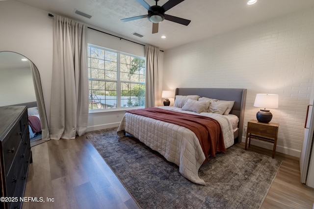 bedroom featuring baseboards, brick wall, visible vents, and wood finished floors