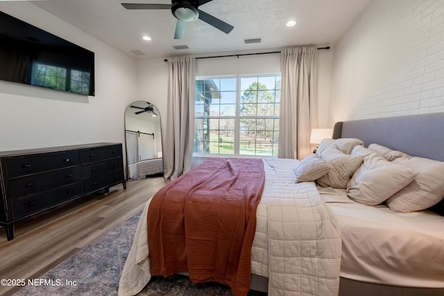 bedroom featuring ceiling fan, brick wall, wood finished floors, and visible vents