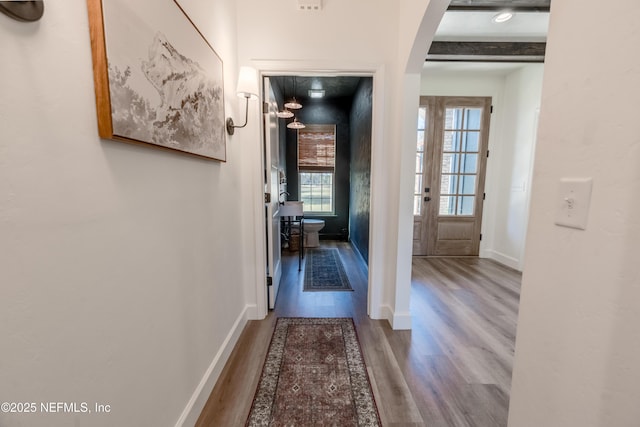 hall with arched walkways, beamed ceiling, baseboards, and wood finished floors