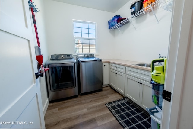 laundry area with light wood finished floors, washer and clothes dryer, a sink, and cabinet space