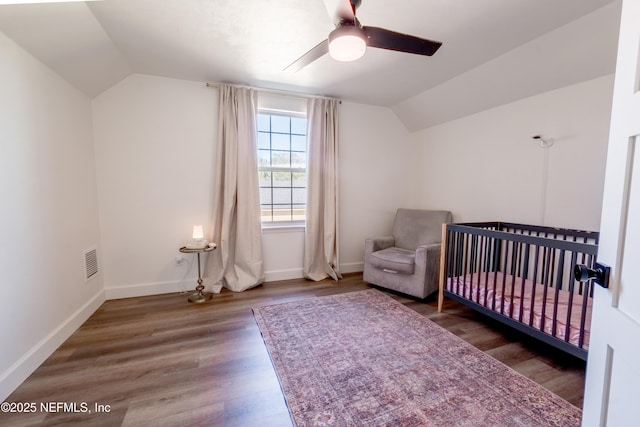 bedroom featuring lofted ceiling, visible vents, wood finished floors, a crib, and baseboards