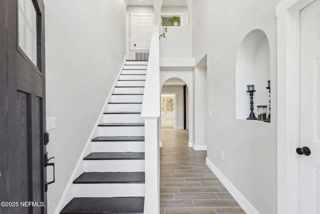 staircase with visible vents, arched walkways, baseboards, wood tiled floor, and a high ceiling