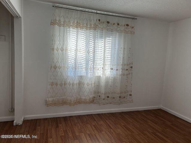 unfurnished room with baseboards, dark wood-style flooring, and a textured ceiling