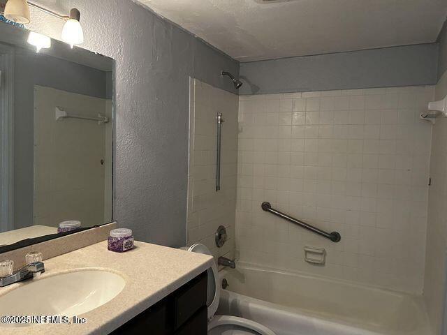 bathroom with toilet, bathtub / shower combination, vanity, and a textured wall