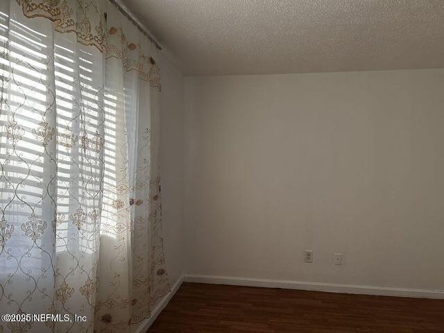 spare room with dark wood-style floors, a textured ceiling, and baseboards