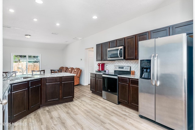 kitchen with light wood finished floors, a sink, stainless steel appliances, dark brown cabinets, and backsplash