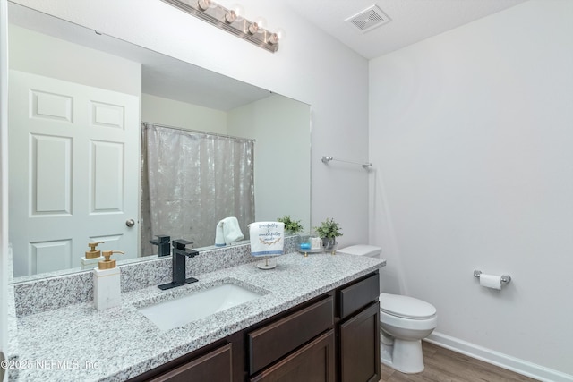 bathroom featuring baseboards, visible vents, toilet, wood finished floors, and vanity