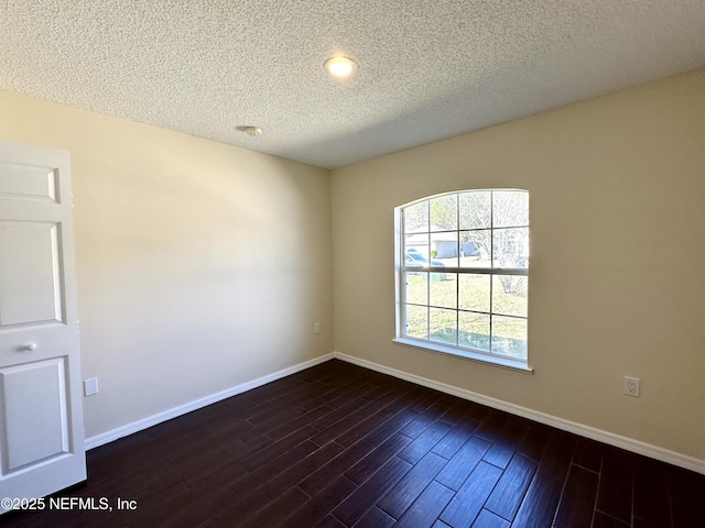 empty room with a textured ceiling, dark wood finished floors, and baseboards