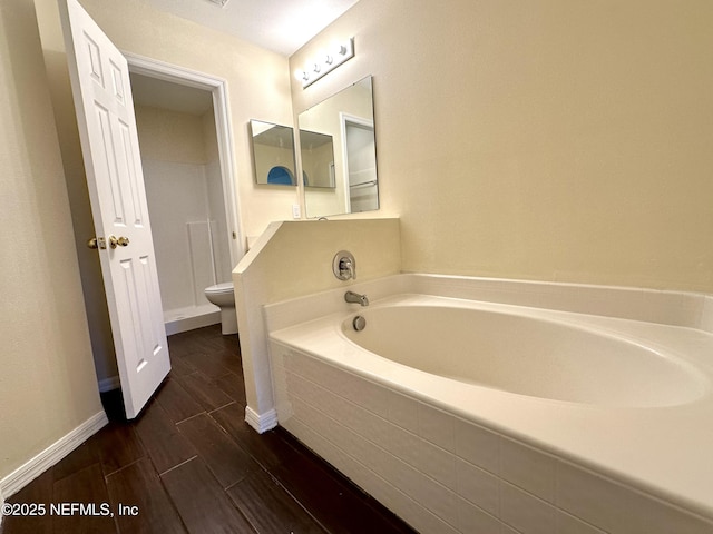 full bath featuring toilet, baseboards, a bath, and wood finished floors