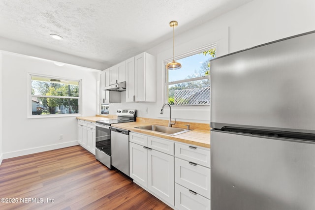 kitchen featuring stainless steel appliances, under cabinet range hood, white cabinetry, pendant lighting, and a sink