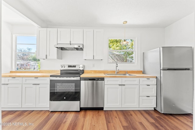 kitchen with appliances with stainless steel finishes, wood counters, white cabinetry, and under cabinet range hood